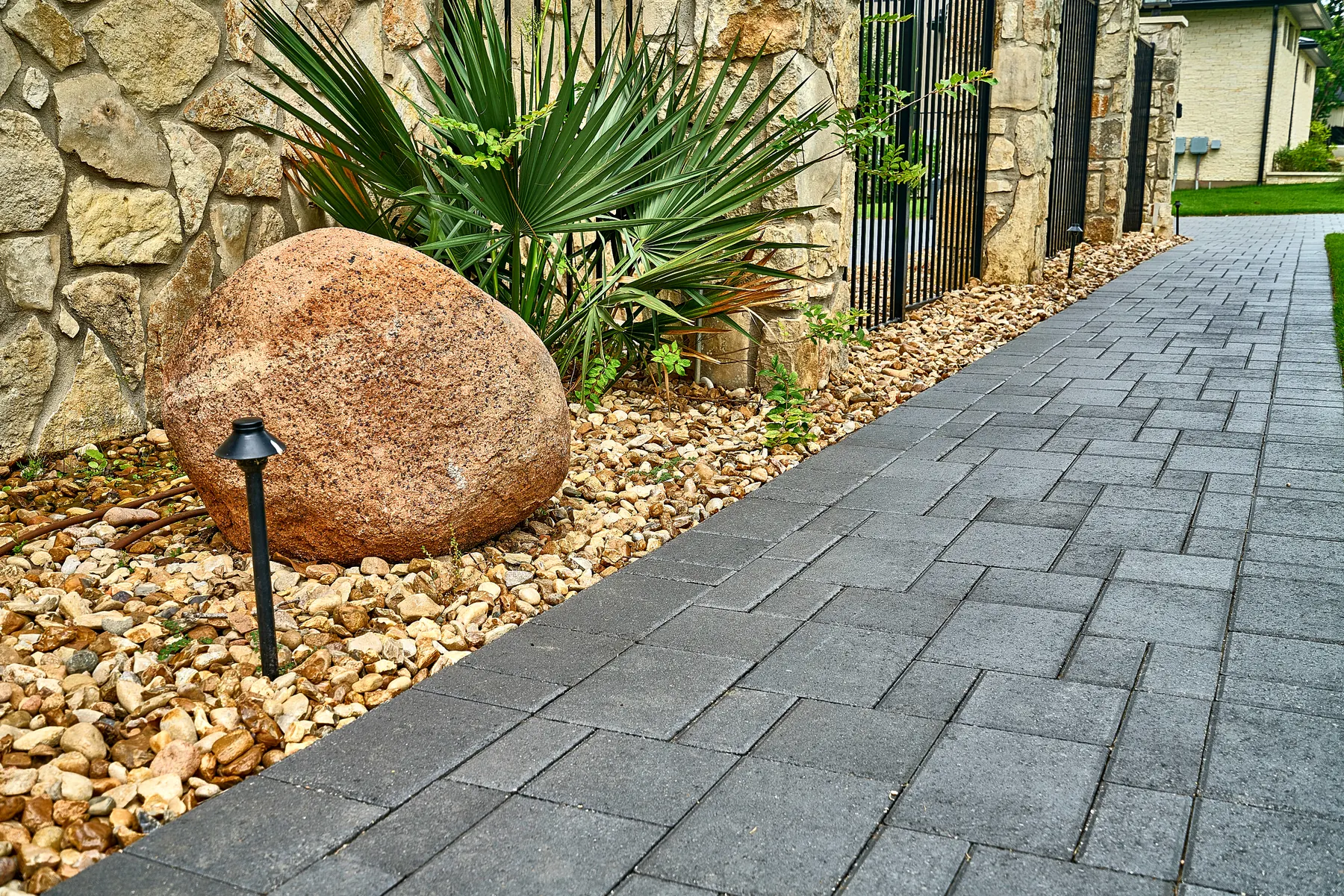 Charcoal-bordered paver walkway with stone wall and river-rock bed